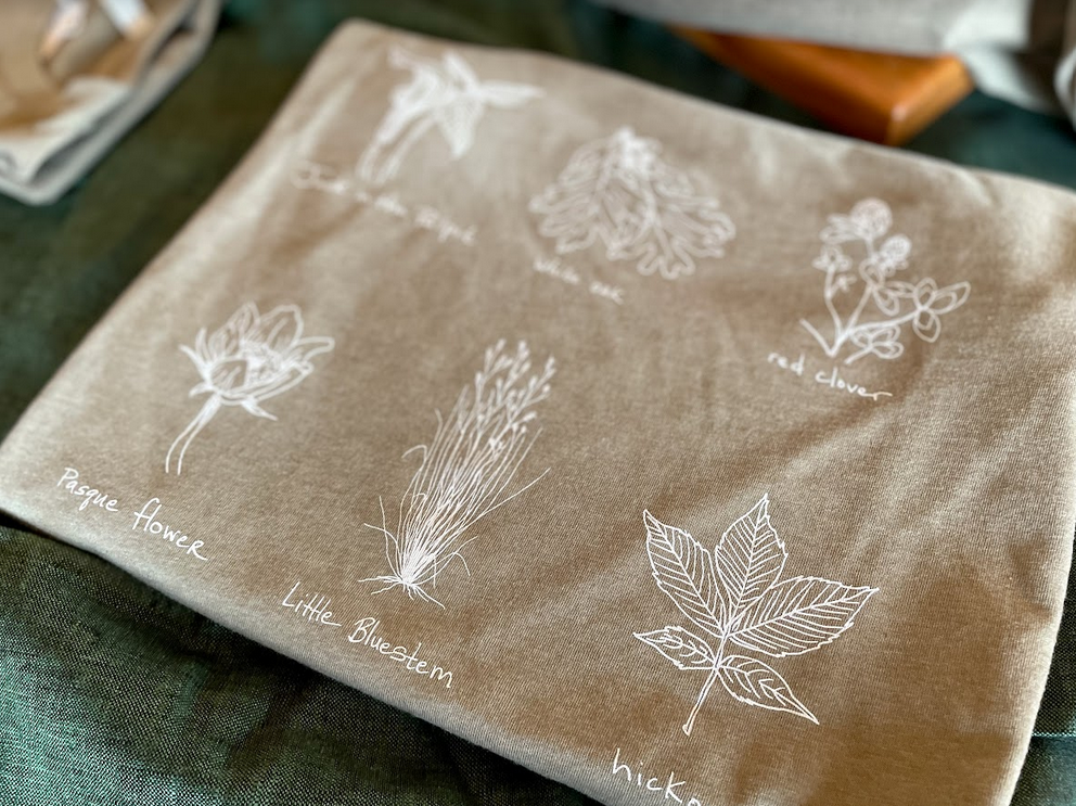 Olive green t-shirt design depicting six illustrations of plants found at Taliesin. Photo depicting three holiday ornaments hanging from branches. Recommended in the Taliesin 2021 Gift Guide. Photo depicting three holiday ornaments hanging from branches. Recommended in the Taliesin 2021 Gift Guide. Recommended in the 2021 Gift Guide.